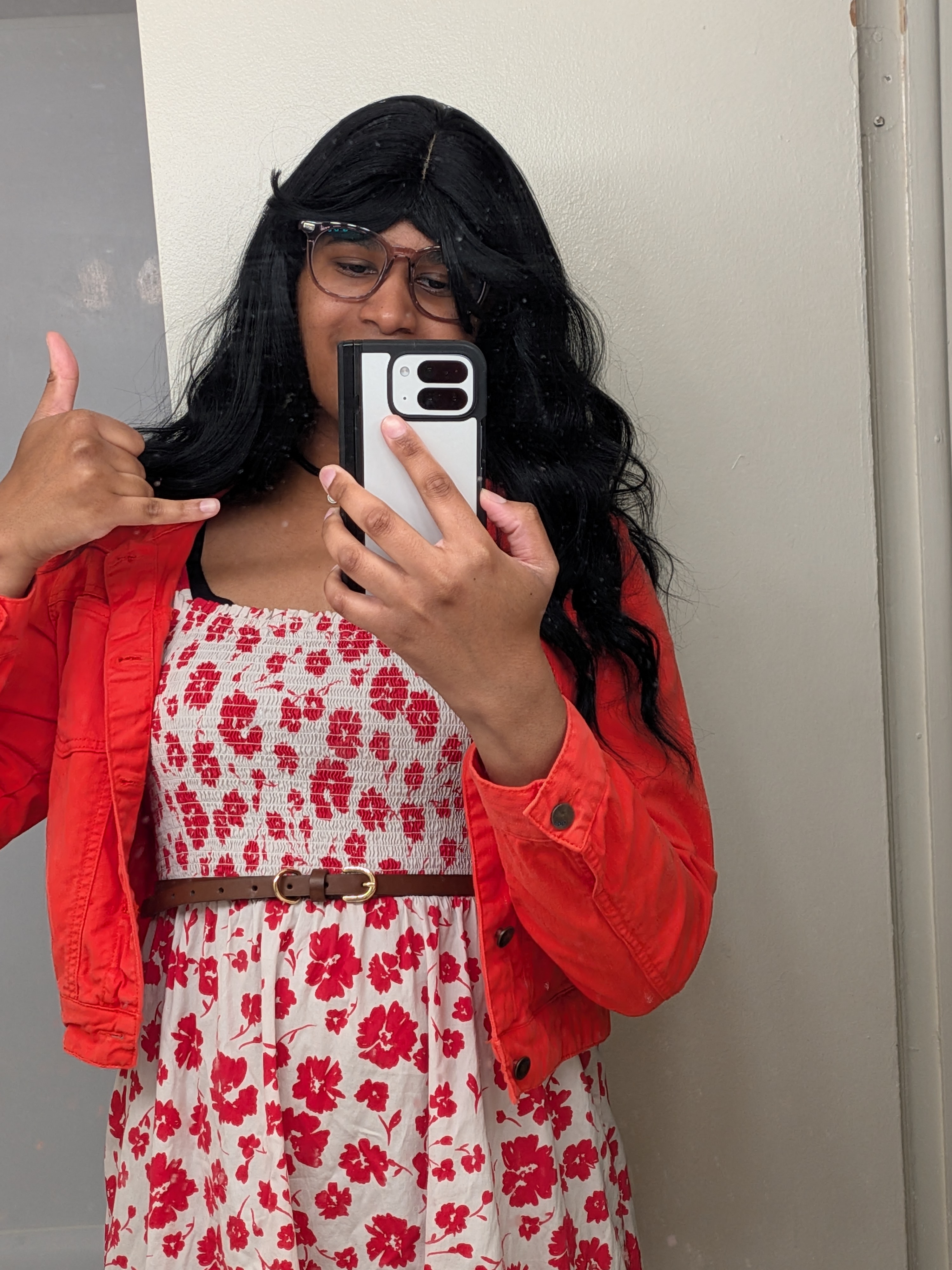 Adrianna wearing a long red maxi dress thats white with a red floral pattern, a thin brown belt, and a red jean jacket